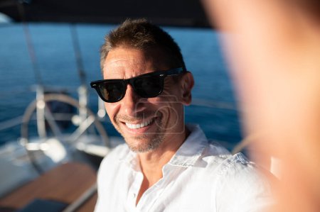 Foto de Feliz viajero. Feliz sonriente hombre maduro en gafas de sol viajando en un yate - Imagen libre de derechos