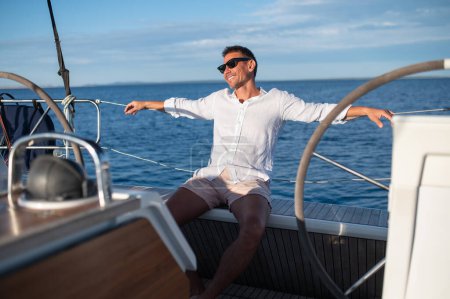 Téléchargez les photos : Joyeux voyageur. Heureux homme mûr souriant en lunettes de soleil voyageant sur un yacht - en image libre de droit