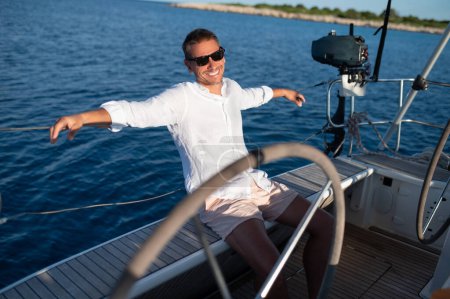 Téléchargez les photos : Joyeux voyageur. Heureux homme mûr souriant en lunettes de soleil voyageant sur un yacht - en image libre de droit