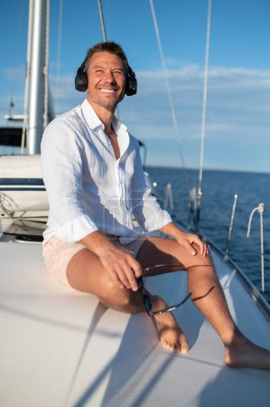 Téléchargez les photos : Sur un yacht. Homme heureux dans les écouteurs écouter de la musique tout en naviguant sur un yacht - en image libre de droit