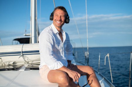 Téléchargez les photos : Sur un yacht. Homme heureux dans les écouteurs écouter de la musique tout en naviguant sur un yacht - en image libre de droit