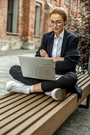 Photo for Working. Young woman in eyeglasses sitting with her legs crossed and working on laptop - Royalty Free Image