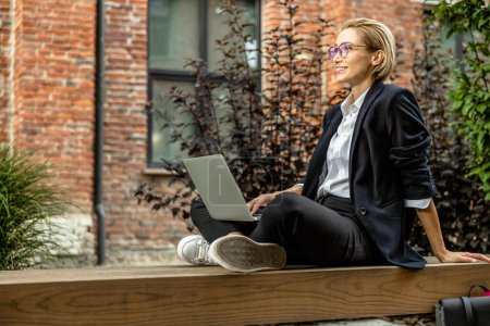 Photo for Working remotely. Pretty young woman in eyeglasses working on laptop outside - Royalty Free Image