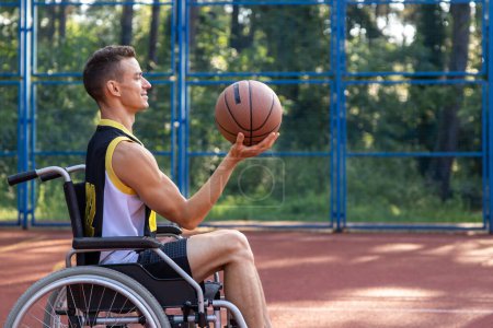 Foto de Jugador de baloncesto caucásico feliz con discapacidad utiliza silla de ruedas mientras juega en la cancha de deportes al aire libre. - Imagen libre de derechos