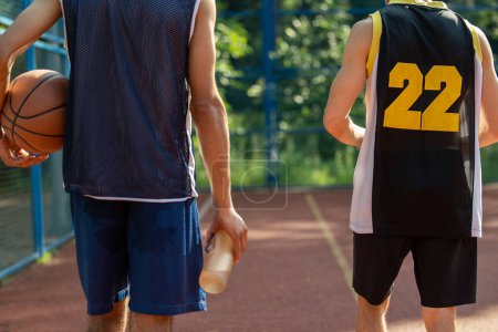 Foto de Hombres irreconocibles amigos jugadores caminando en la cancha de baloncesto al aire libre. - Imagen libre de derechos