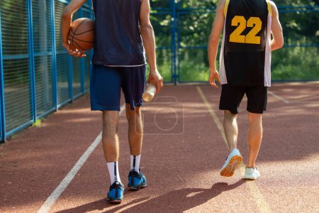 Téléchargez les photos : Hommes méconnaissables amis joueurs marchant sur le terrain de basket en plein air. - en image libre de droit