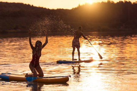 Téléchargez les photos : Silhouette de jeune femme et homme surfant sur la planche SUP à travers la surface de l'eau. - en image libre de droit