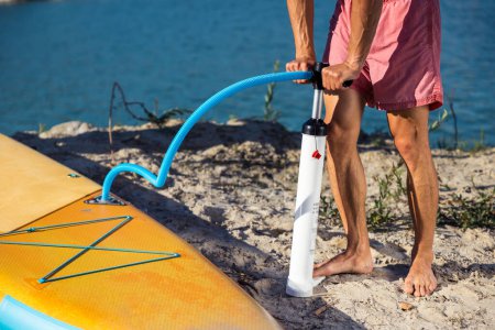 Téléchargez les photos : Homme méconnaissable préparant SUPboard jaune pour le surf, loisirs actifs. - en image libre de droit