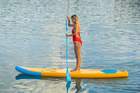 Photo for Beautiful woman with paddle on sub board floating on the water in the sea. - Royalty Free Image