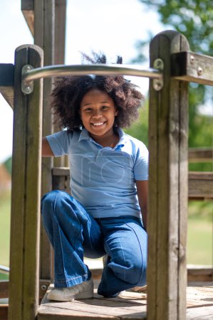 Photo for In the park. Smiling cute dark-skinned girl looking happy and contented whle playing in park - Royalty Free Image