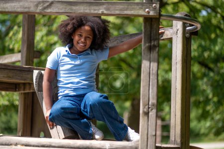Foto de En el parque. Sonriendo linda chica de piel oscura buscando feliz y contento whle jugando en el parque - Imagen libre de derechos