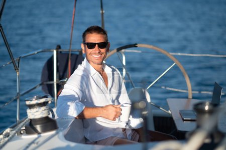 Téléchargez les photos : Café du matin. Satisfait homme en lunettes de soleil assis sur un pont de yacht avec une tasse de café - en image libre de droit