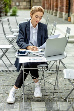 Téléchargez les photos : Nomade numérique. Femme d'affaires assise à la table dans un café de rue et travaillant - en image libre de droit