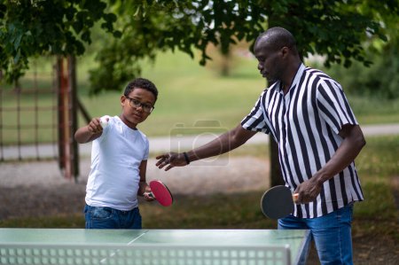 Téléchargez les photos : Tennis de table. Papa jouant au tennis de table avec son fils dans le parc - en image libre de droit