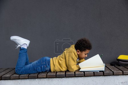 Foto de Haciendo los deberes. Colegial en sudadera con capucha amarilla mirando involucrado mientras hace la tarea - Imagen libre de derechos