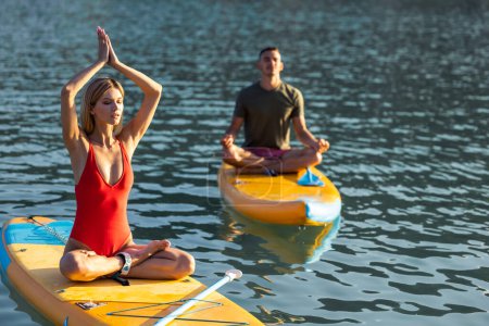 Téléchargez les photos : Homme et femme pratiquant le yoga sur la planche à soup, activité sportive d'été familiale moderne. - en image libre de droit