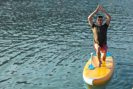 Photo for Man practicing yoga on SUP board on river. - Royalty Free Image