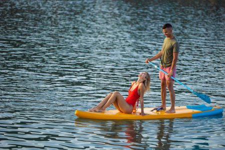 Téléchargez les photos : Femme active et l'homme surfant dans l'océan sur la planche à soup ar vacances d'été. - en image libre de droit