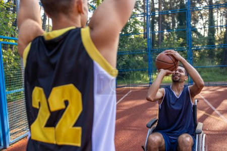 Photo for Athlete man in wheelchair and his friend enjoying playing basketball outdoors. - Royalty Free Image