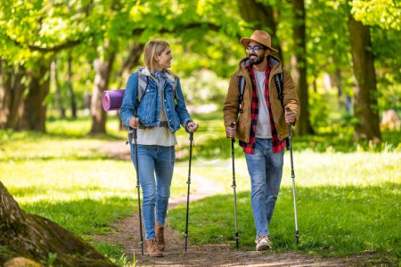 Photo for Couple in the park. Young couple with scandinavian sticks walking and talking - Royalty Free Image