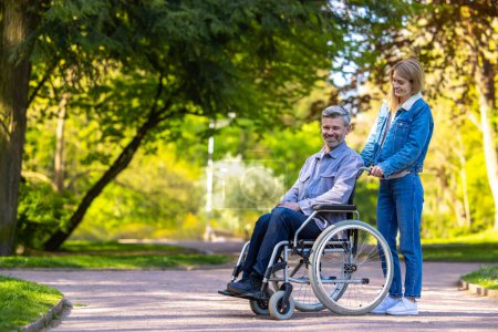 Téléchargez les photos : Joyeux couple. Homme en fauteuil roulant se promenant dans le parc avec sa femme - en image libre de droit