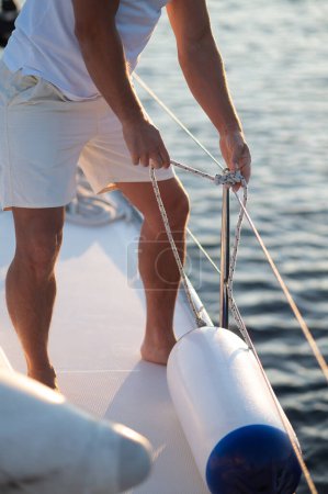 Téléchargez les photos : Yachting. Homme en vêtements blancs fixant des cordes sur un yacht - en image libre de droit