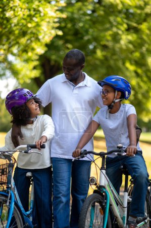 Foto de Fin de semana familiar. Familia afroamericana pasando un buen rato en un parque y montando bicicletas - Imagen libre de derechos