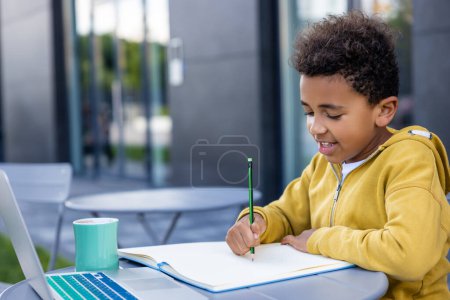 Téléchargez les photos : Un écolier. mignon afro-américain garçon faire des leçons et regarder satisfait - en image libre de droit
