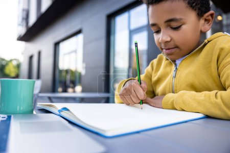 Téléchargez les photos : Un écolier. mignon afro-américain garçon faire des leçons et regarder satisfait - en image libre de droit