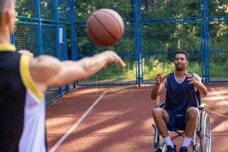 Téléchargez les photos : Sportsman en fauteuil roulant et compagnon s'amuser avec le basketball en plein air. - en image libre de droit