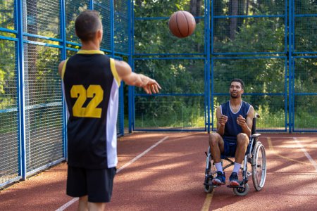 Photo for Wheelchair athlete man and companion in high spirits during outdoor basketball. - Royalty Free Image