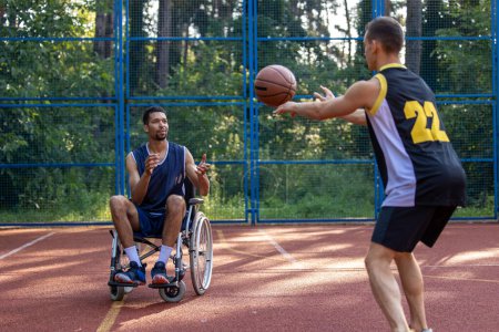Téléchargez les photos : Athlète en fauteuil roulant homme et ami trouver la joie dans le basketball en plein air. - en image libre de droit
