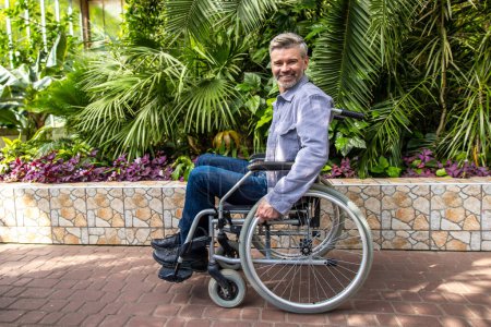 Photo for Man on a wheelchair in the park. Gray-hiared man on a wheelchair in a park - Royalty Free Image