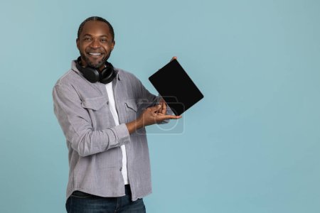 Foto de Hombre negro alegre mostrando tableta pantalla vacía para contenido promocional aislado sobre fondo azul - Imagen libre de derechos
