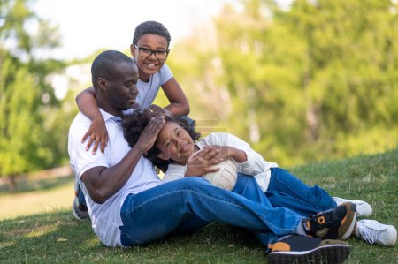 Photo for Family time. Dad and two kids sitting on the grass in the park - Royalty Free Image
