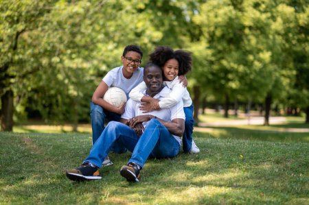 Téléchargez les photos : Du temps en famille. Papa et deux enfants assis sur l'herbe dans le parc - en image libre de droit