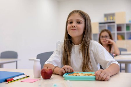 Foto de Hora del almuerzo. Linda chica de pelo largo almorzando en la escuela - Imagen libre de derechos