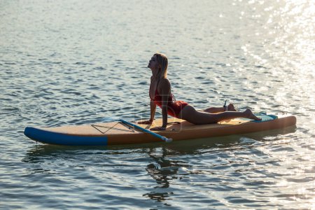 Foto de Mujer atractiva practicando yoga en sup board en agua de mar. - Imagen libre de derechos