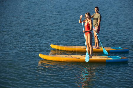 Téléchargez les photos : Paddleboard plage femme et homme surf en mer sur planche de surf, couple faisant du sport nautique. - en image libre de droit