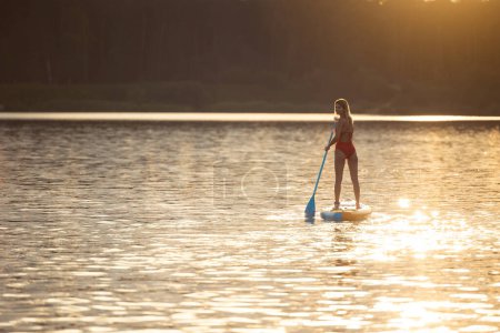 Téléchargez les photos : Jeune femme surfant au lever du soleil sur la rivière ou le lac. - en image libre de droit