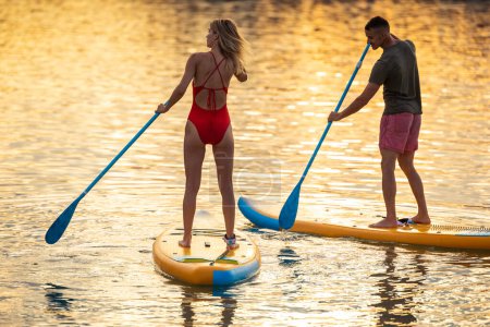 Photo for Man and woman paddle sup board surfers at sunset. - Royalty Free Image