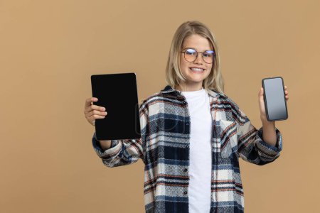 Téléchargez les photos : Adolescent moderne. Blonde teen en lunettes avec tablette et smartphone dans les mains - en image libre de droit