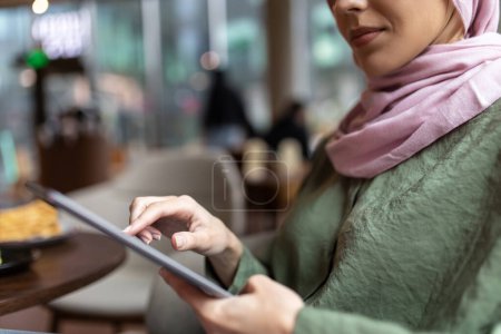 Téléchargez les photos : Nomade numérique. Jeune femme en hijab travaillant dans un café et regardant satisfait - en image libre de droit