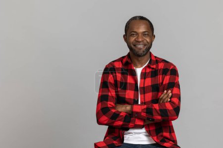 Photo for Smiling black bearded man wearing red checkered shirt keeps hands folded posing isolated over gray studio background. - Royalty Free Image