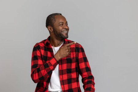 Photo for Positive black bearded man wearing red checkered shirt pointing at advertisement area posing isolated over gray studio background. - Royalty Free Image