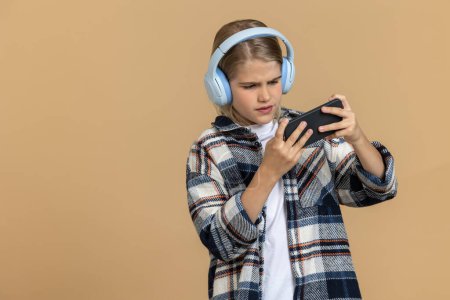 Téléchargez les photos : Adolescent avec un téléphone. Adolescent dans un casque avec un smartphone dans les mains - en image libre de droit
