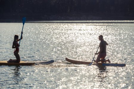 Foto de Pareja feliz hombre y mujer flota en el río en supboards puesta de sol, deporte de estilo de vida de verano por diversión. - Imagen libre de derechos