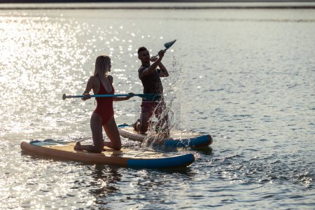 Téléchargez les photos : Happy couple homme et femme flotte sur la rivière sur les planches coucher de soleil, sport de style de vie d'été pour le plaisir. - en image libre de droit