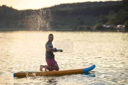 Photo for Man on the supboard on the middle of the lake at sunset. - Royalty Free Image