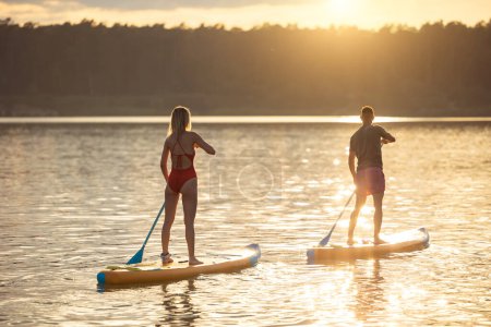 Photo for Man and woman paddle sup board surfers at sunset. - Royalty Free Image